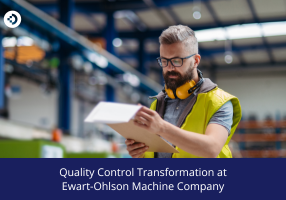 Person in a high‑visibility vest reviewing a clipboard in a large industrial facility, representing quality control transformation at Ewart‑Ohlson Machine Company.