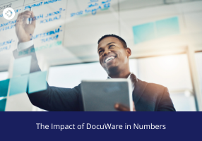 Person writing on a glass board filled with handwritten notes while holding a tablet, illustrating the impact of DocuWare in numbers.